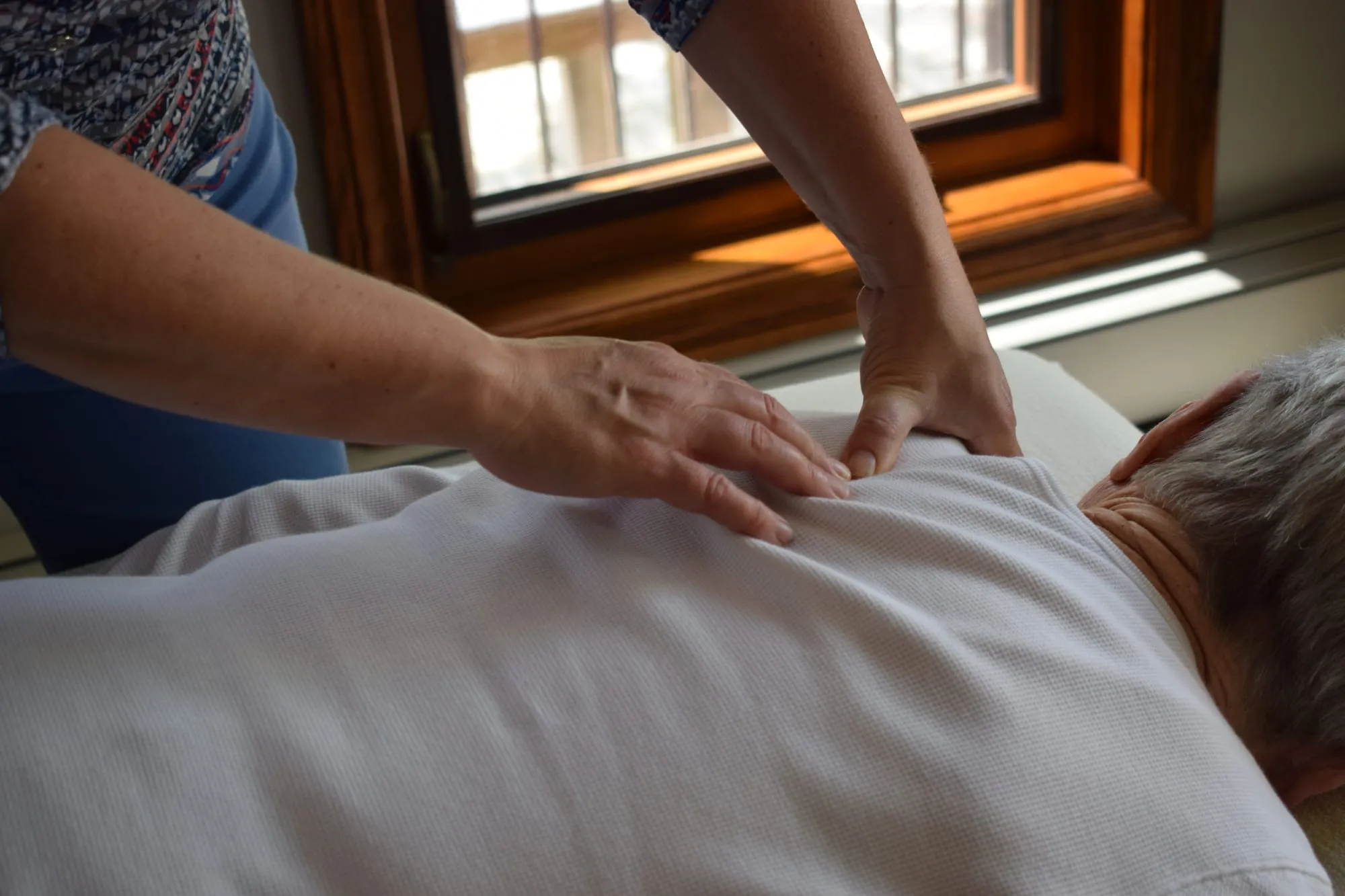 Carol's hands working gently on a client's back through their clothing during a Bowen session